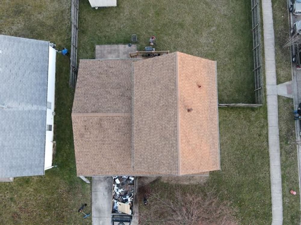 Aerial view of a house with a brown roof and surrounding grass, near a pile of debris.