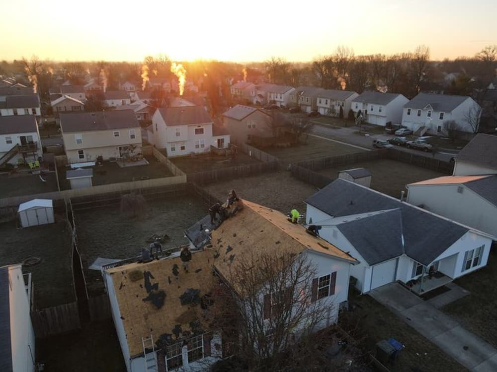 Roofing contractors installing new shingles at sunset over residential neighborhood.