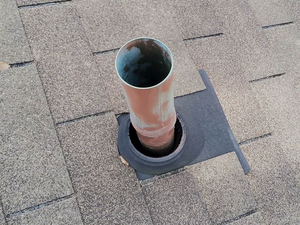 Vent pipe on a shingle roof, showing rust and surrounding seals for weatherproofing.