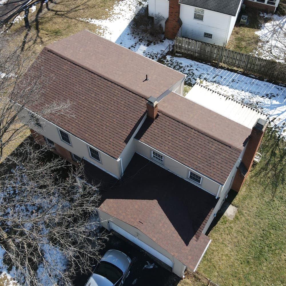 Aerial view of a residential home with a shingled roof and snow in the yard.
