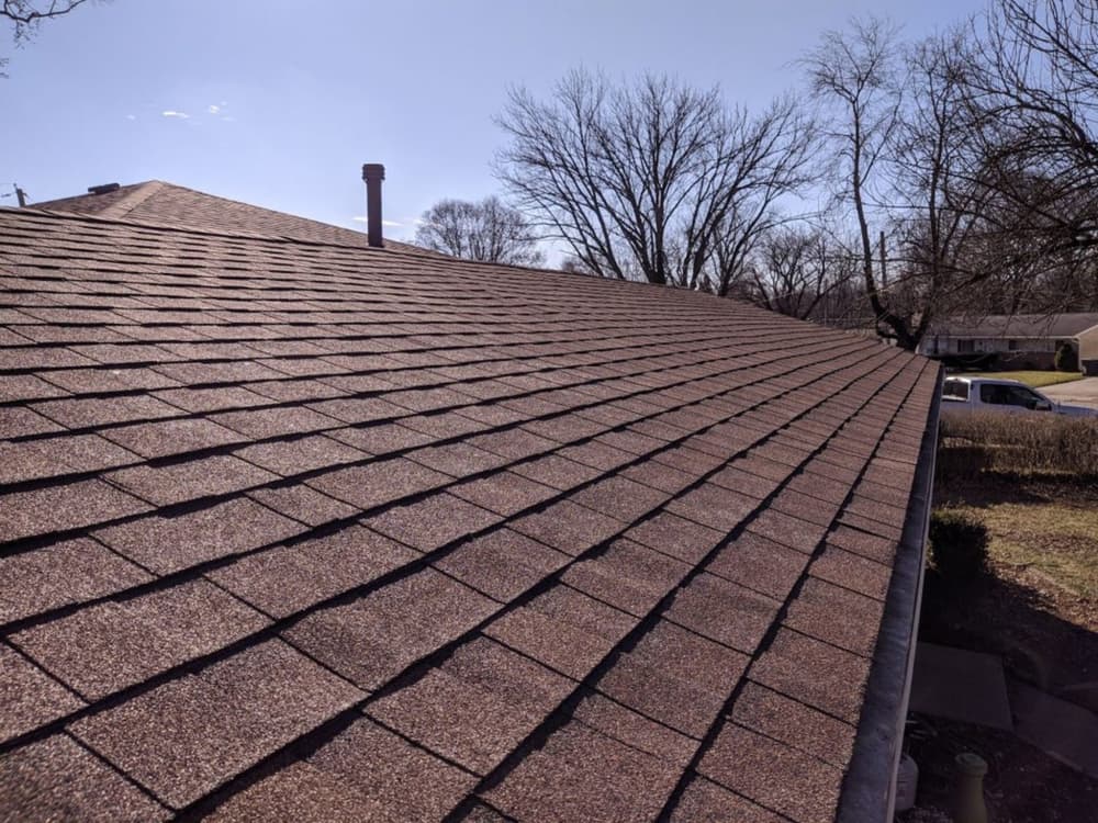 Brown asphalt shingles on a sloped roof under a clear blue sky.