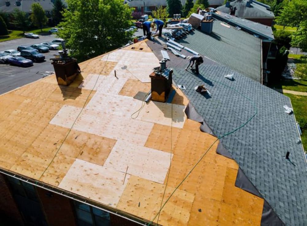 Roofing contractors installing shingles on a residential building under blue skies.