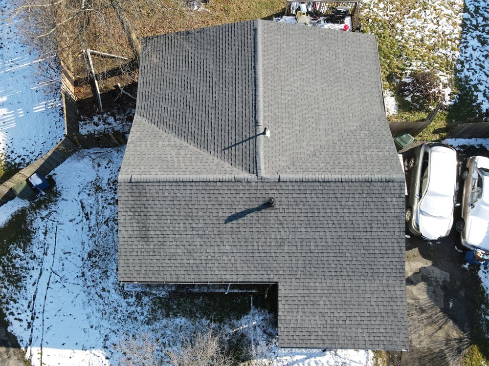 Aerial view of a house roof with dark shingles and snow around the edges.