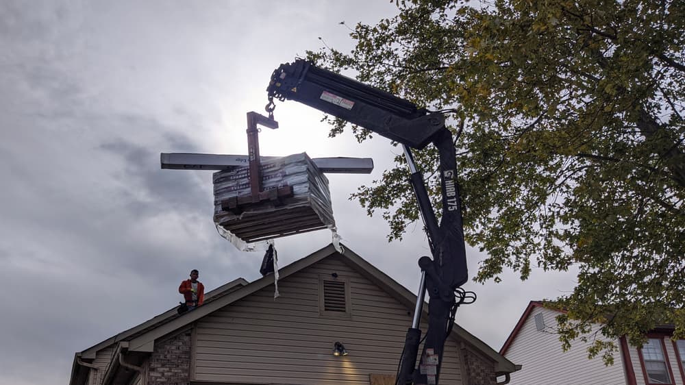 Construction worker unloading materials from a crane onto a roof during daylight.