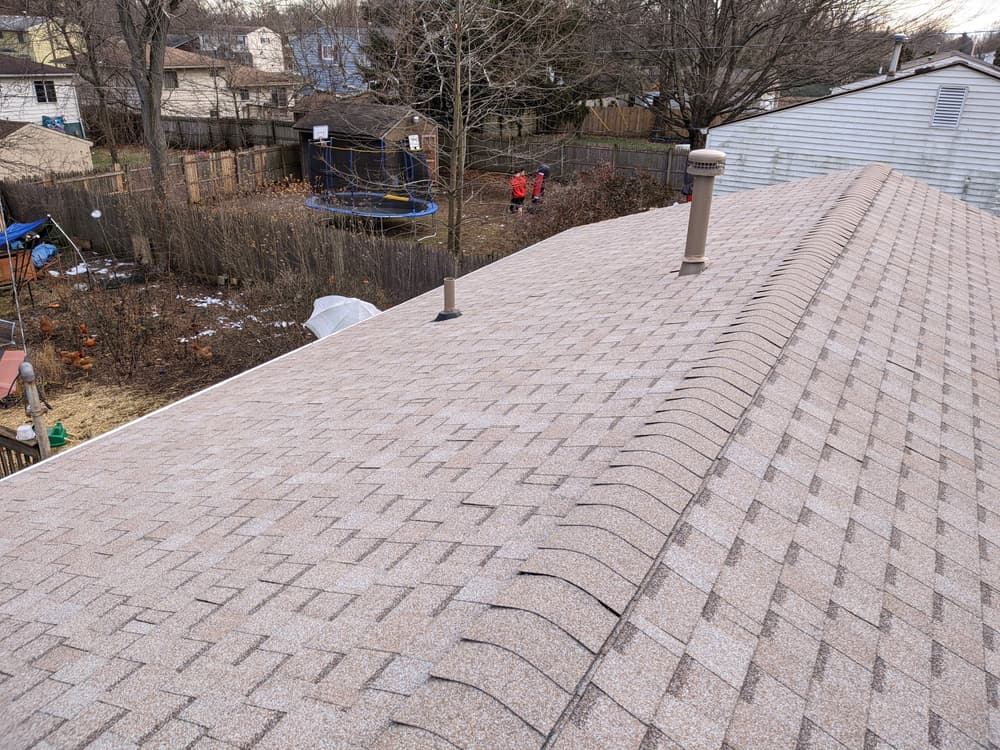 Aerial view of a residential roof with shingles, overlooking a backyard with a trampoline.