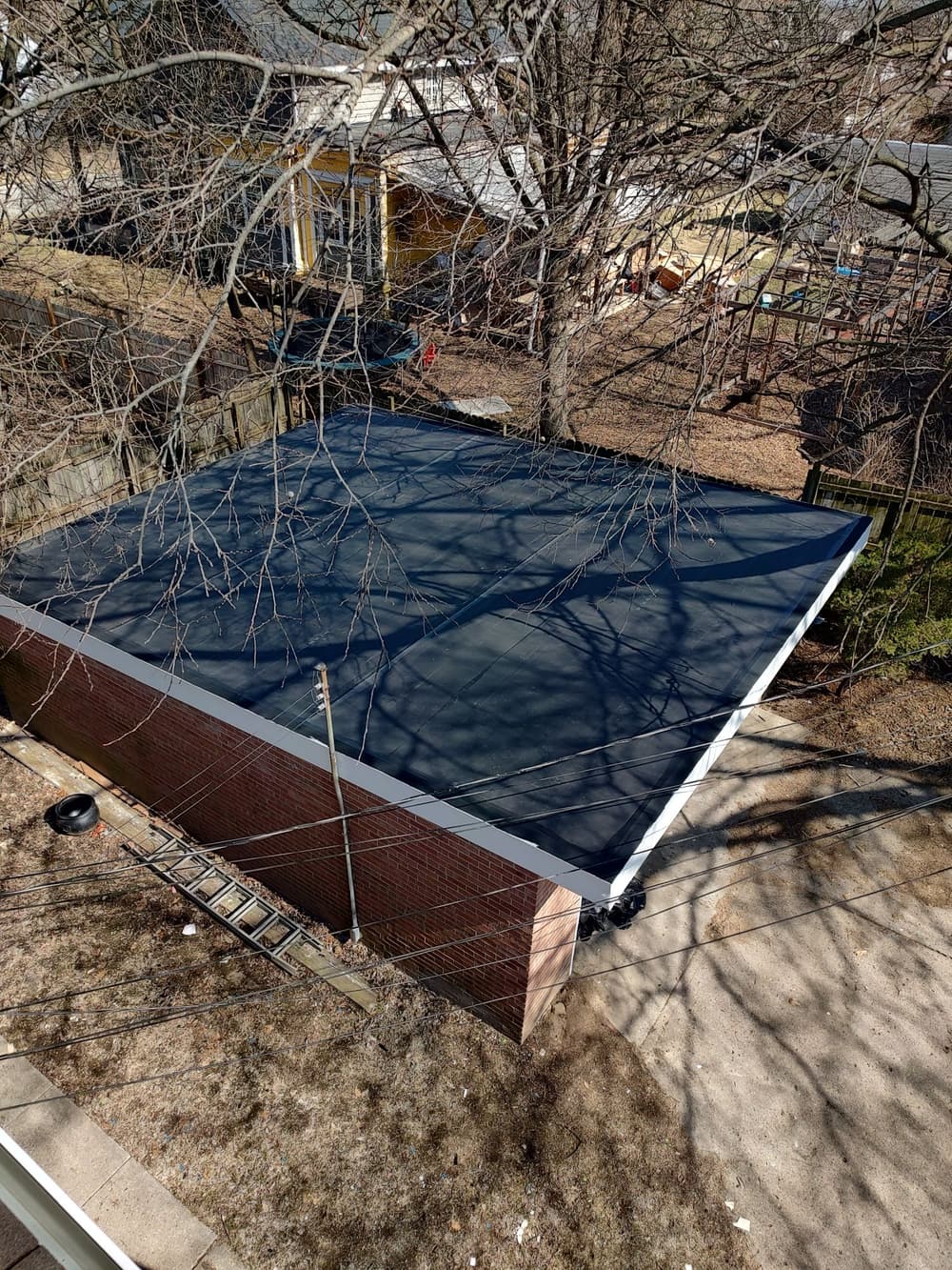 Flat black roof of a garage surrounded by trees and power lines on a suburban street.