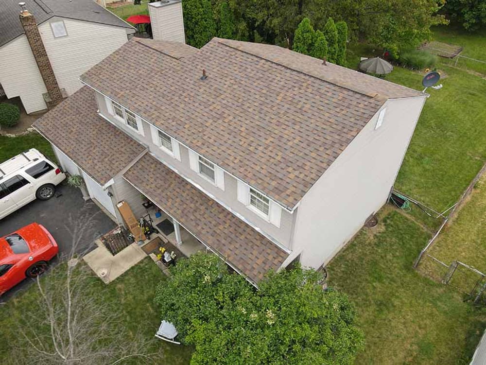 Aerial view of a residential home with a multi-colored shingle roof and green lawn.