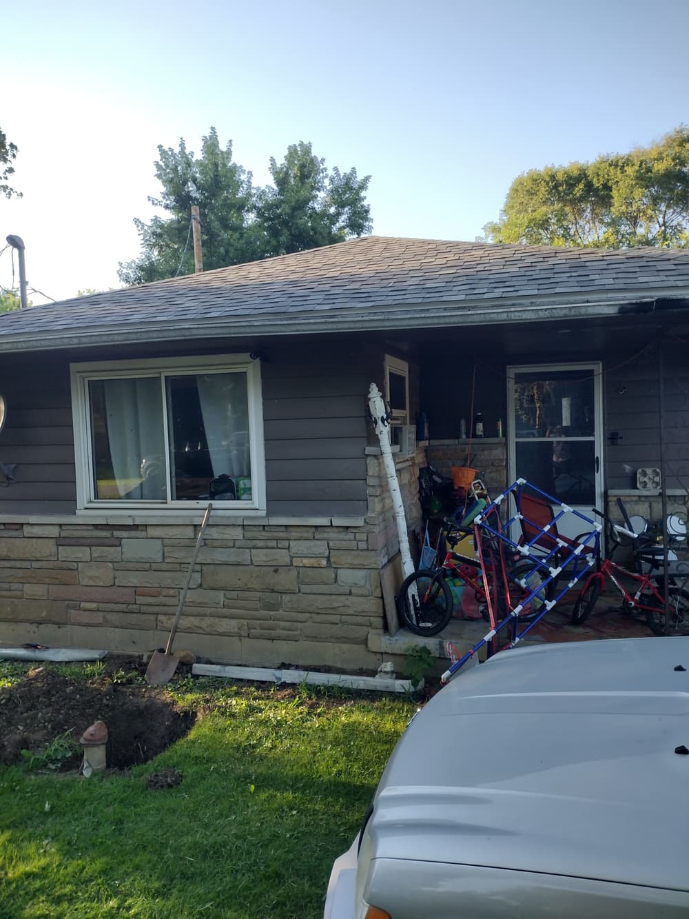 House exterior with stone foundation and bikes stacked in yard, surrounded by green grass.