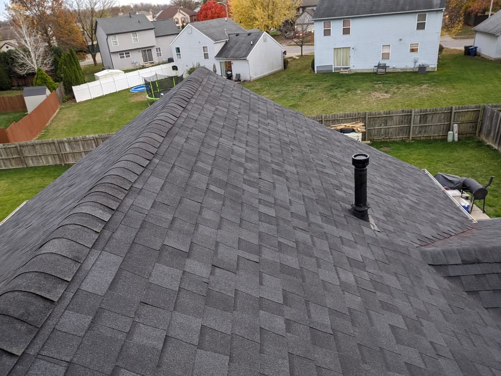 Aerial view of a gray shingle roof with a chimney in a suburban neighborhood.