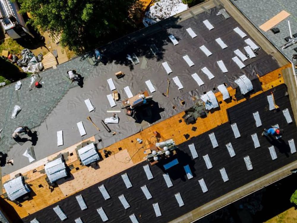 Aerial view of a roof installation with workers applying shingles and materials.