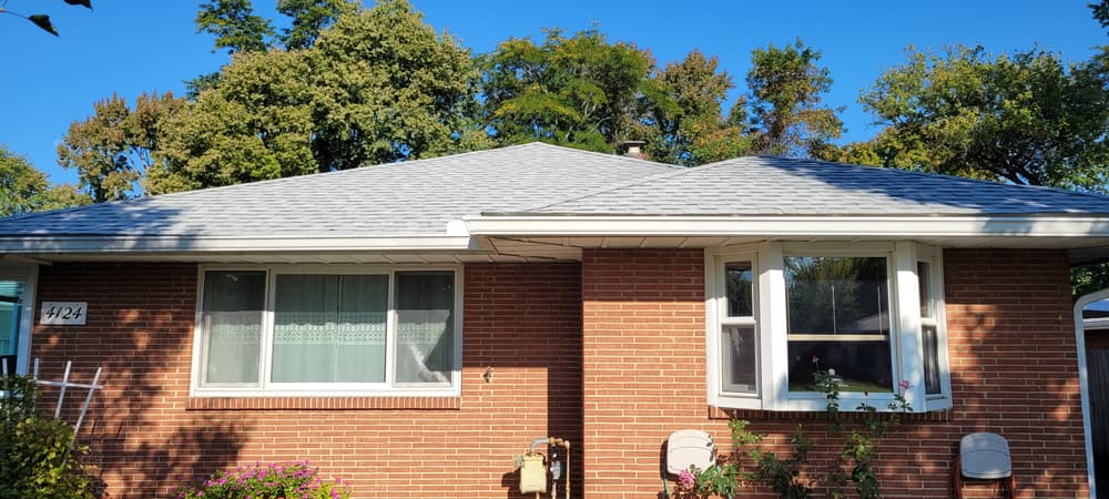 Brick house with a gray shingle roof, bay window, and landscaped garden.