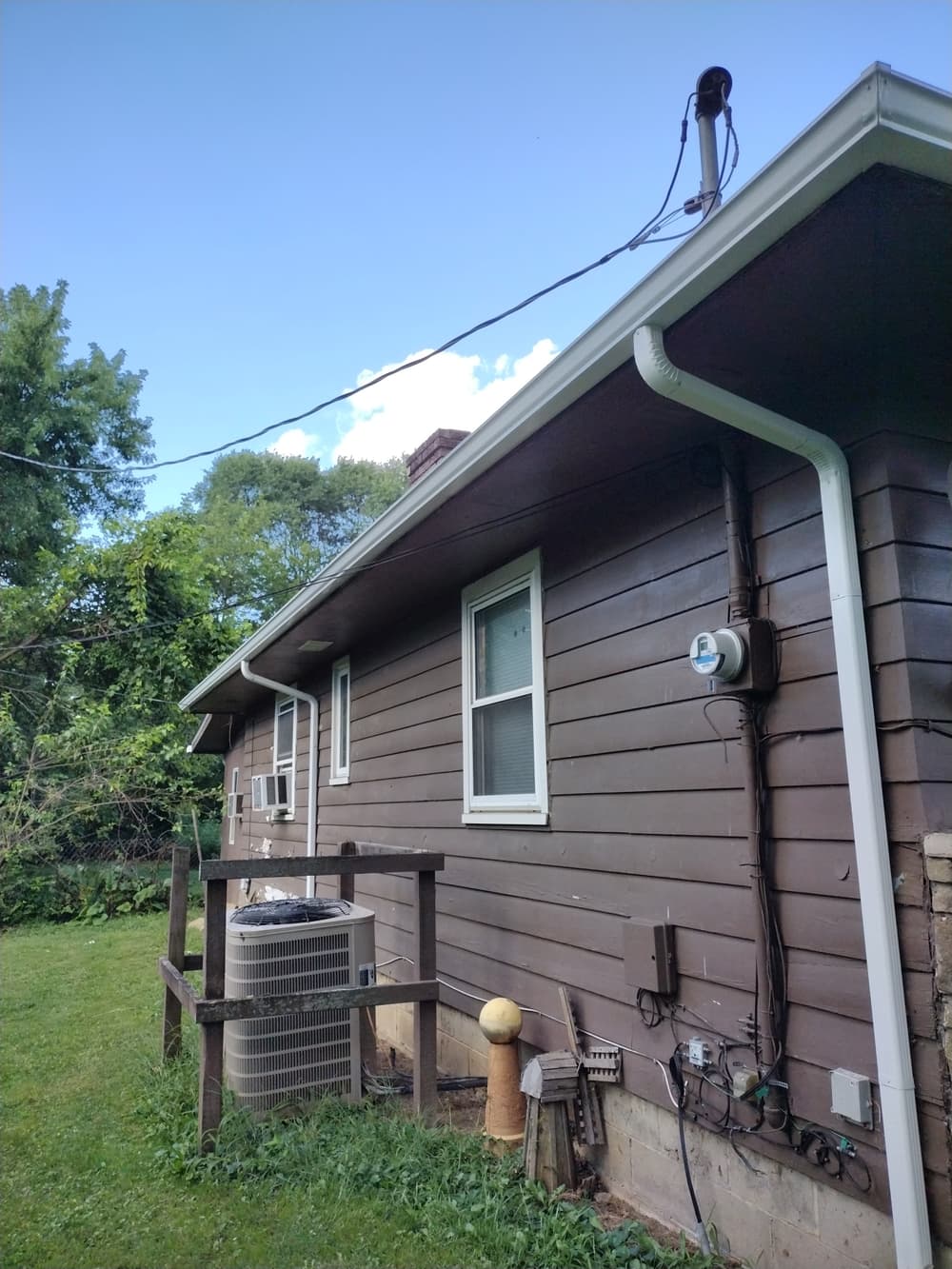 Side view of a brown house with an air conditioner and utility meter in a grassy yard.