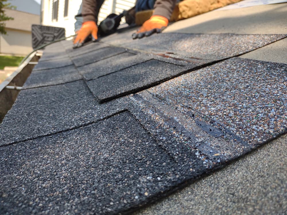 Roofer installing asphalt shingles on residential roof for durable weather protection.