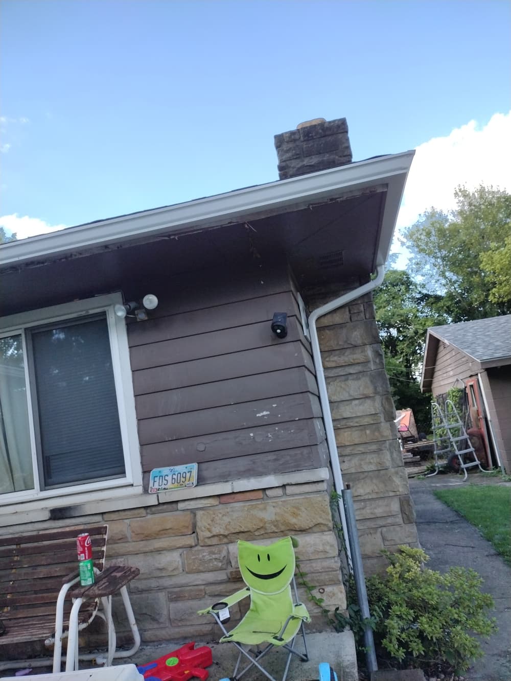House exterior with stone accents, chimney, and a green lawn chair. Clear blue sky above.