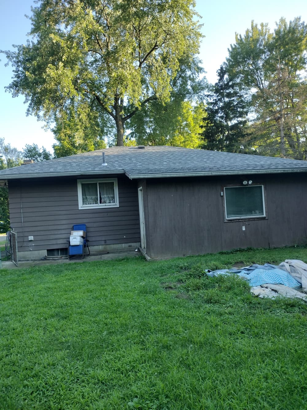 Brown house with a gray roof, surrounded by grass and trees, in a suburban setting.