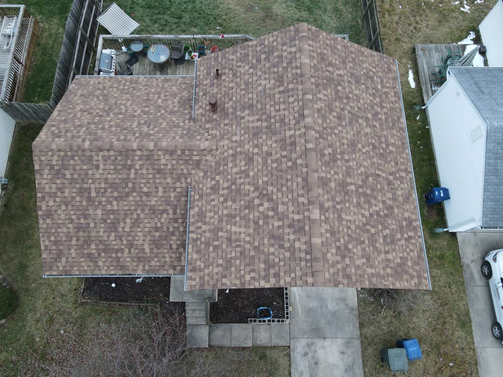 Aerial view of a brown shingled roof on a suburban home with a yard.