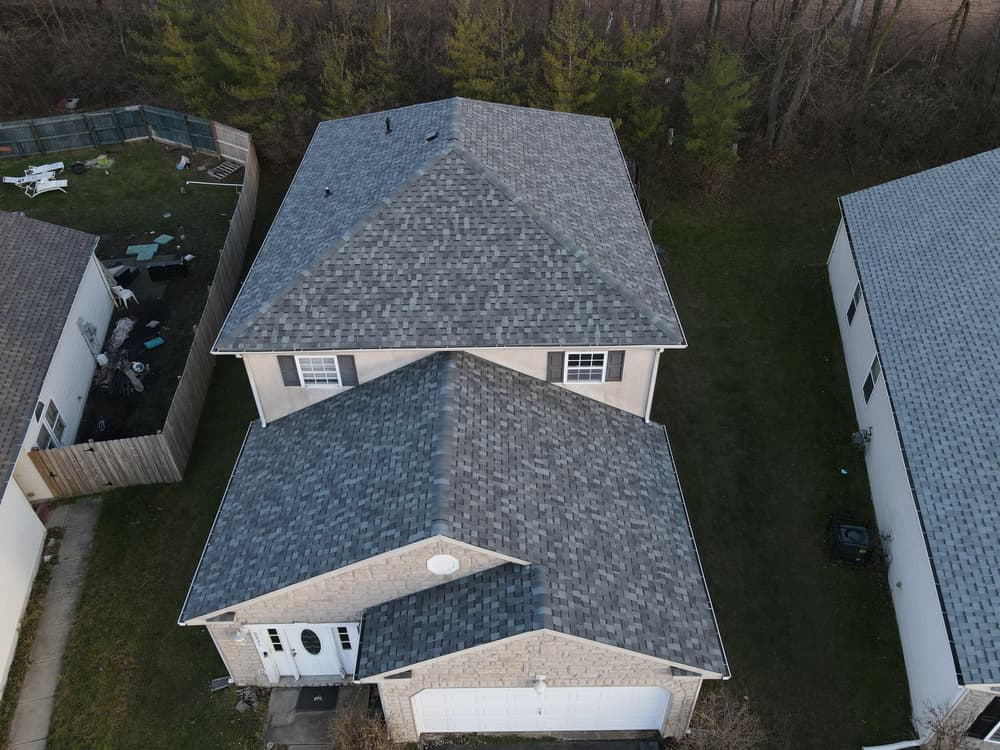 Aerial view of a two-story house with a gray shingle roof and surrounding greenery.