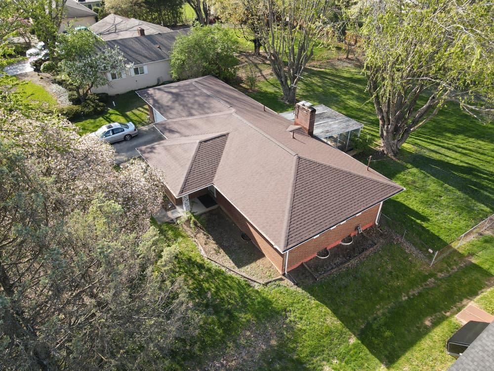 Aerial view of a brick house with a sloped roof and landscaped yard.