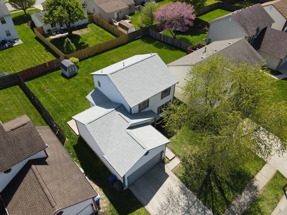 Aerial view of a suburban home featuring a new gray roof and green lawn.