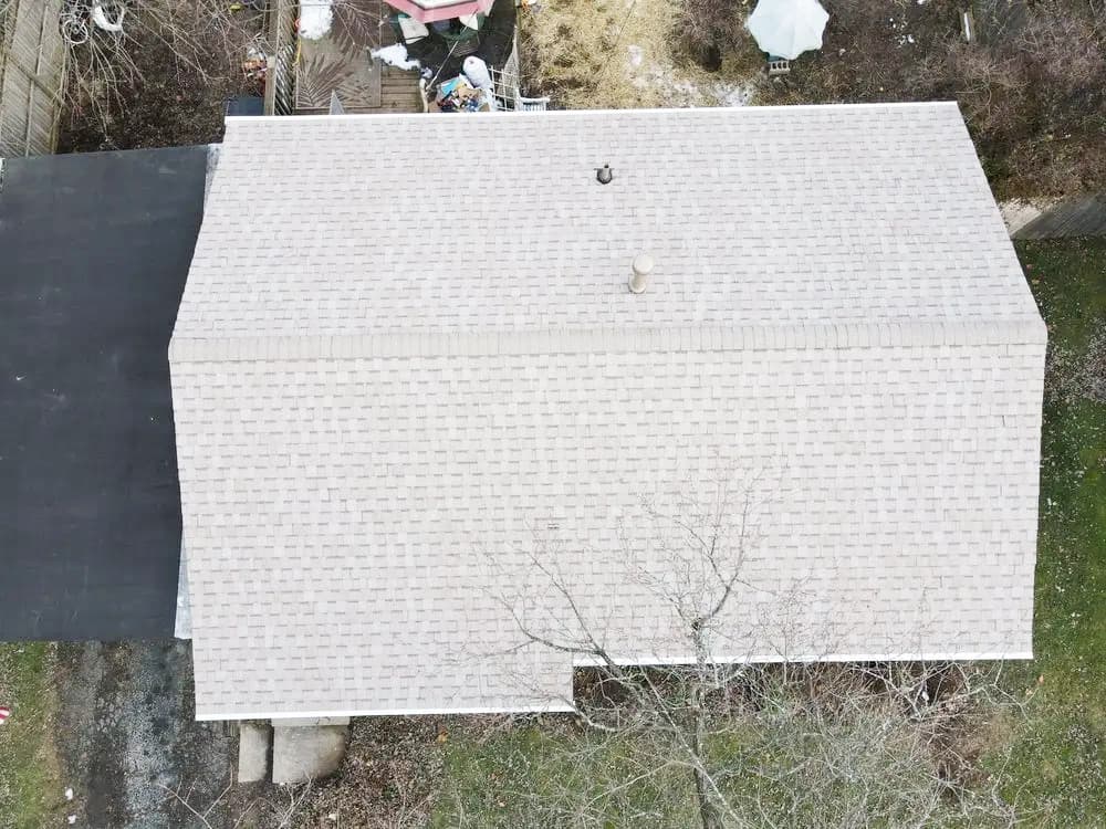 Aerial view of a residential roof with shingles and surrounding greenery.