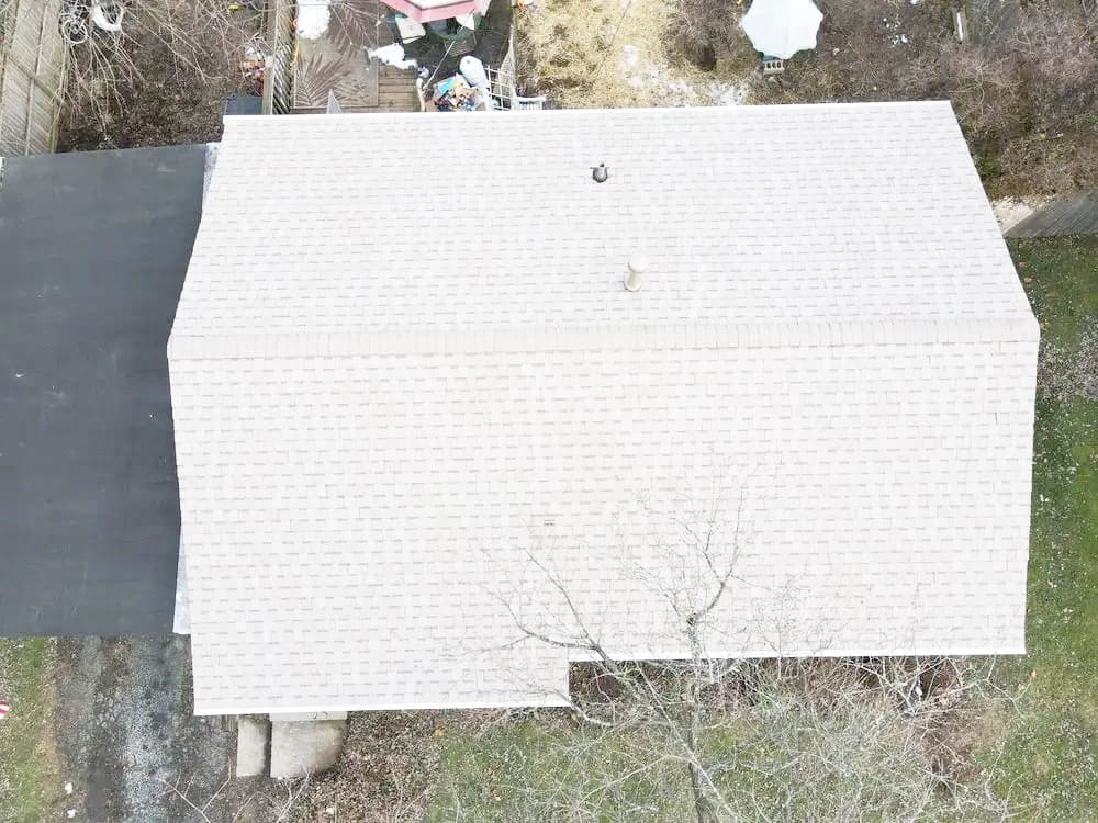 Aerial view of a residential roof with beige shingles and surrounding greenery.