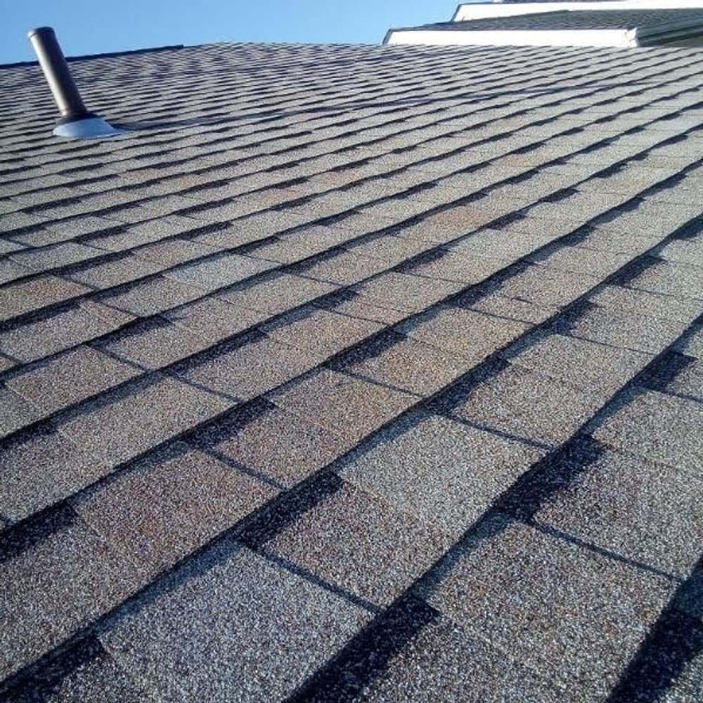 Close-up of a textured asphalt shingle roof with a clear blue sky in the background.