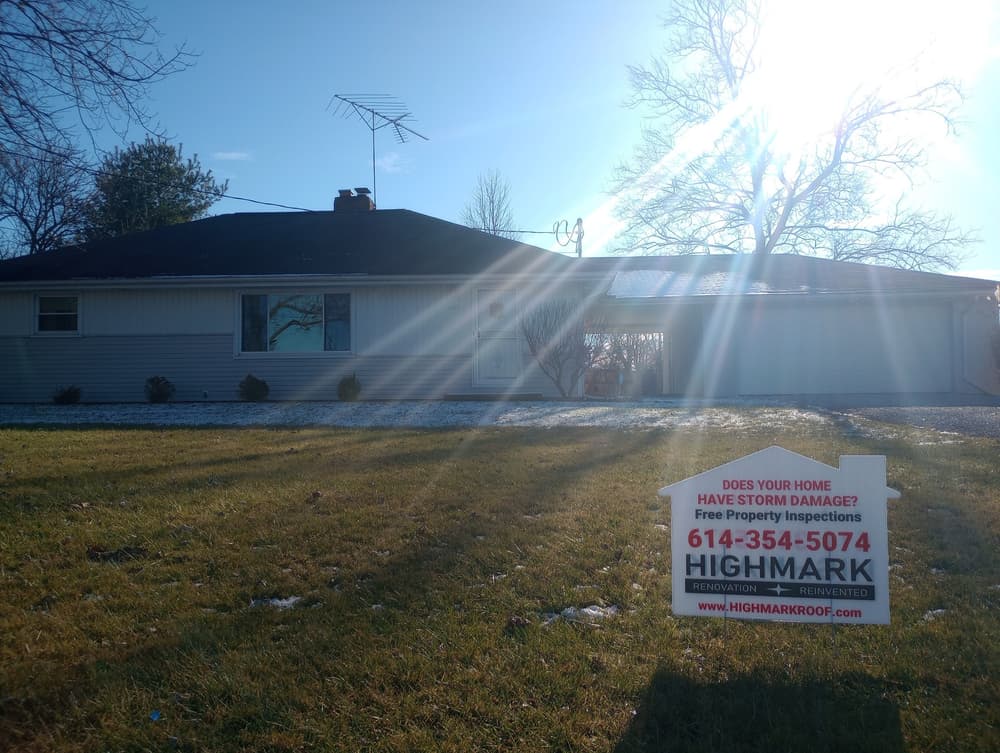 Renovation company sign in front of a house with sun glare and storm damage notice.