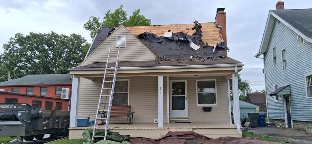 House undergoing roof replacement with contractor on top and tools visible.