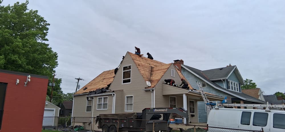 Roofers installing shingles on a residential home under overcast skies.