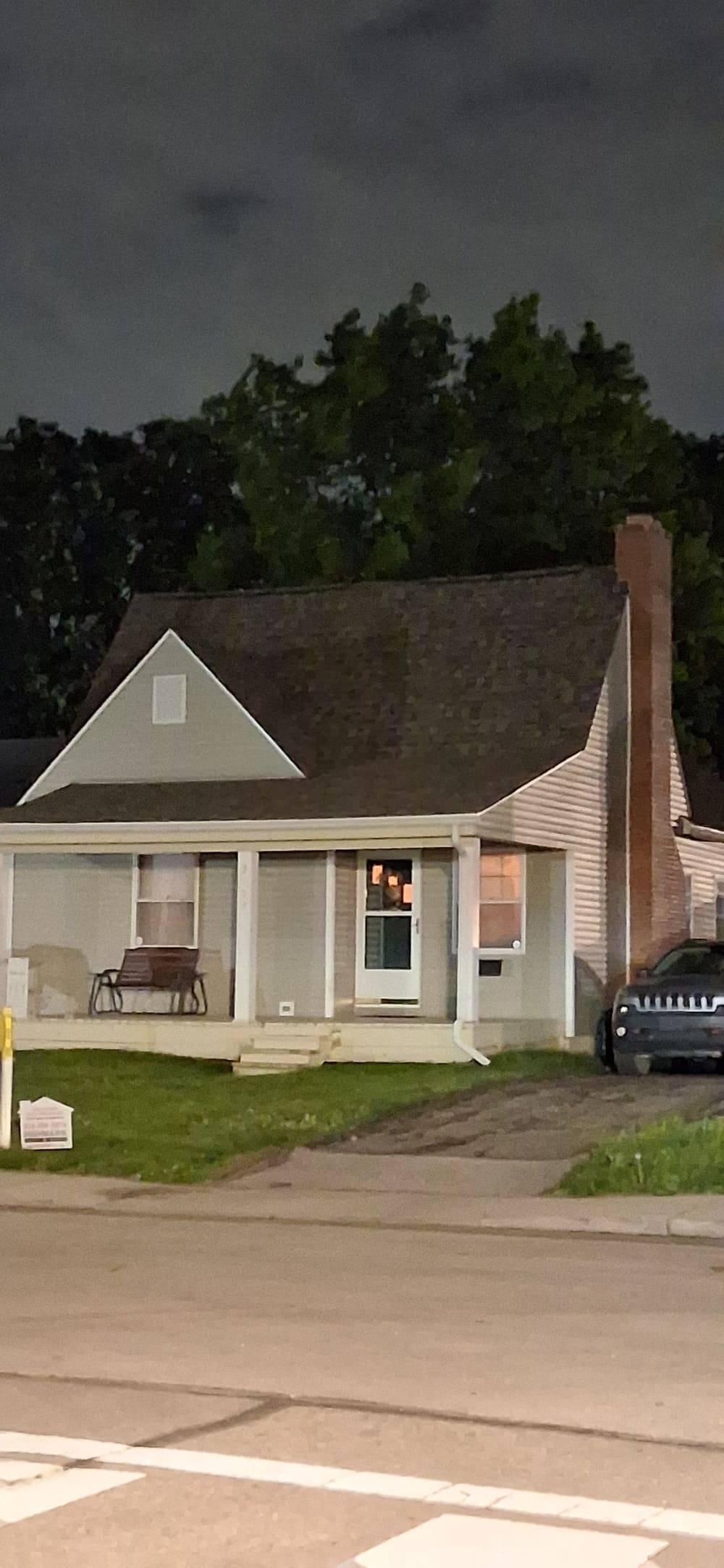 Nighttime view of a cozy house with a porch and a parked car in front.